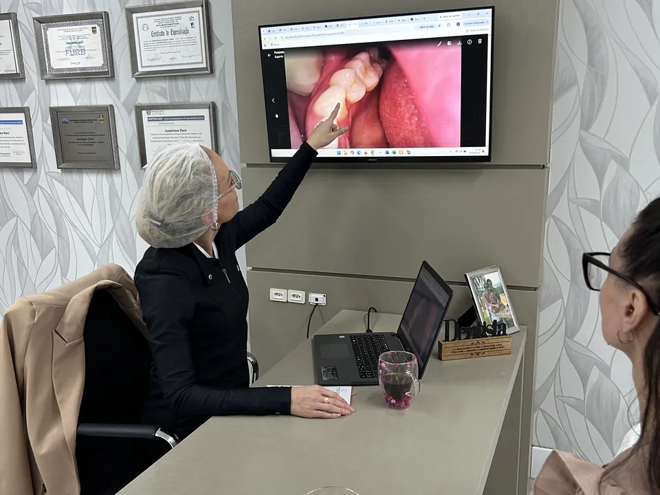 Dra. Jossemare Rech aponta para a imagem da câmera intraoral na tela, apresentando o plano à paciente