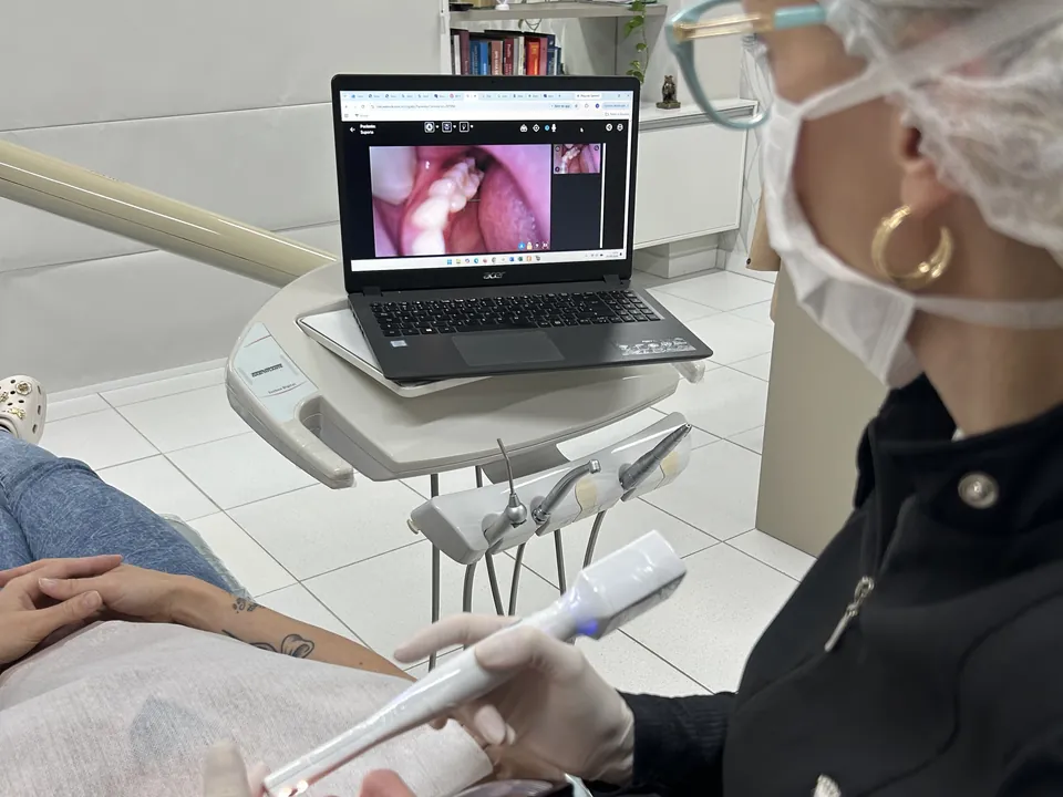 Dra. Jossemare Rech usa a câmera intraoral, com a imagem captada aparecendo na tela do notebook ao lado